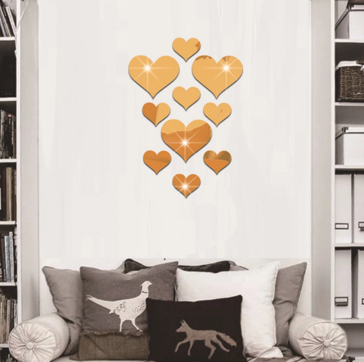 Gold heart-shaped mirror decals on a white wall above a sofa with decorative pillows.