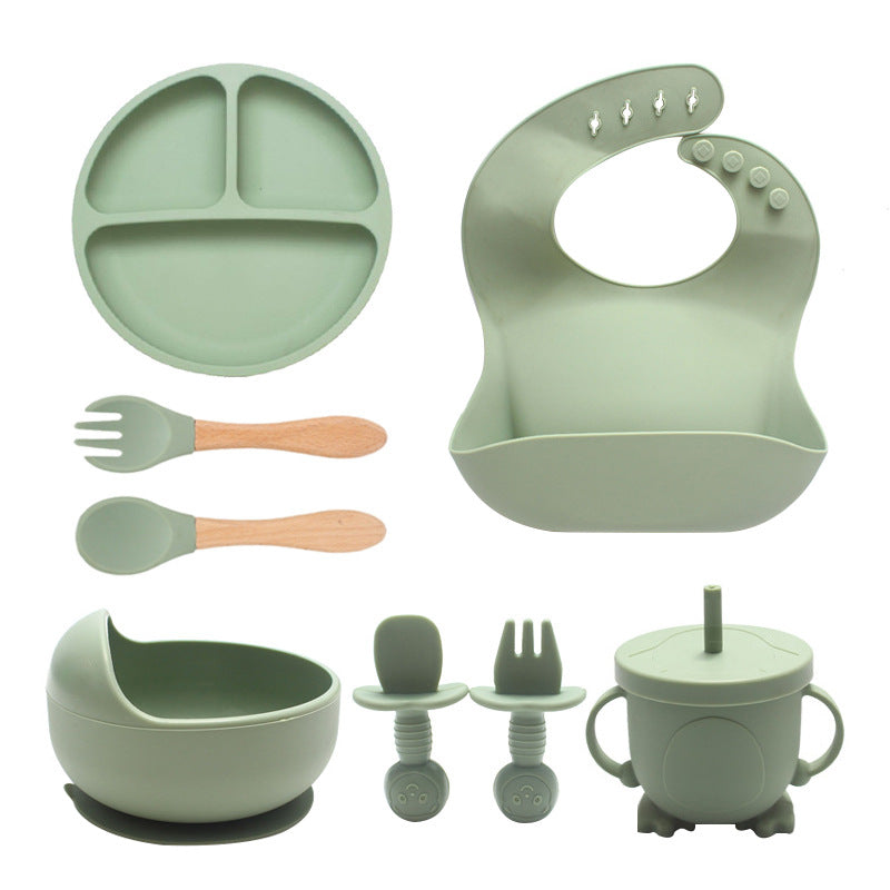 Set of green baby feeding utensils including plate, bib, spoons, fork, bowl, and cup on a white background.
