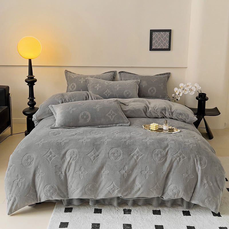 Gray textured comforter with monogram pattern on a bed in a bedroom setting.