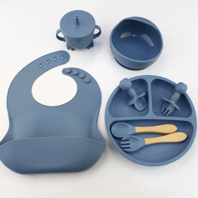 Blue silicone baby feeding set with bib, bowl, spoon, fork, and cup on a white background