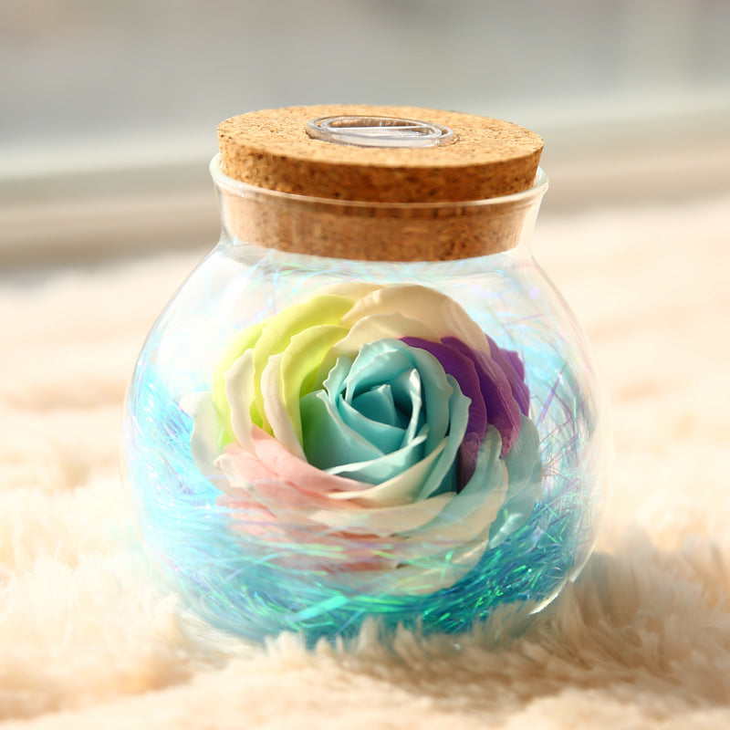 Glass jar with a cork lid containing a multicolored rose on a soft surface.