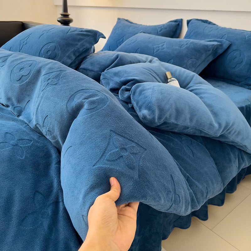 Blue textured comforter with pillows on a bed, held by a hand.