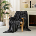 Dark gray textured blanket draped over a wooden chair in a cozy living room with a fireplace.