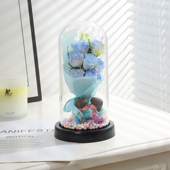 Decorative item with blue roses and figurines inside a glass dome on a white surface.