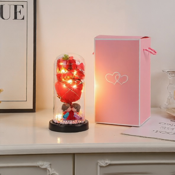 Decorative glass dome with LED lights, small figurines, and a pink gift box on a white surface.