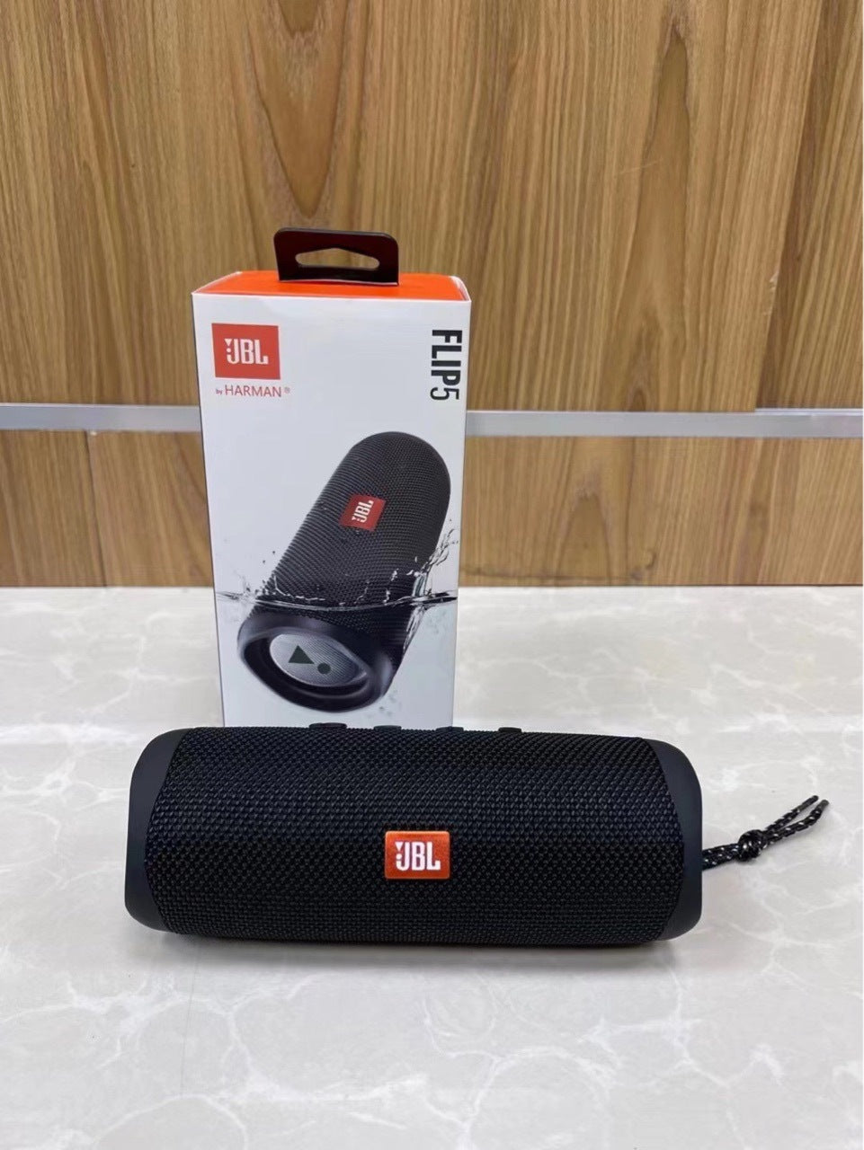 Black JBL Flip 5 portable speaker with packaging on a light gray surface.