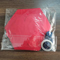 Red silicone mat with blue handle and white tape inside a clear plastic bag on a wooden surface.