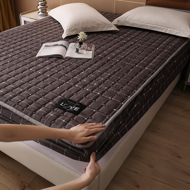 Brown quilted mattress cover on a bed with a hand touching it, in a bedroom setting.