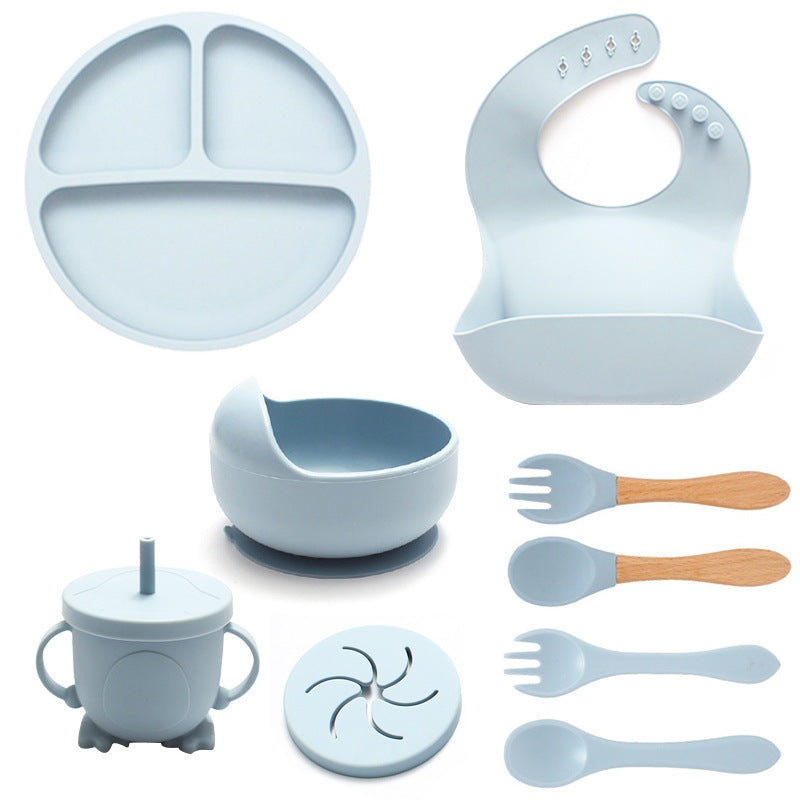Set of baby feeding utensils including a plate, bowl, cup, and bib on a white background.