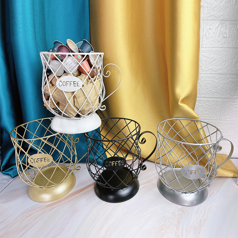 Set of wire coffee capsules holder in gold, black, and silver on a white surface with colorful curtains in the background.