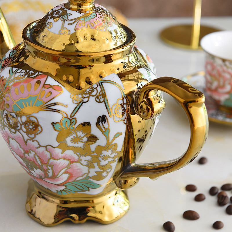 Decorative teapot with floral patterns and gold accents on a white surface with coffee beans.