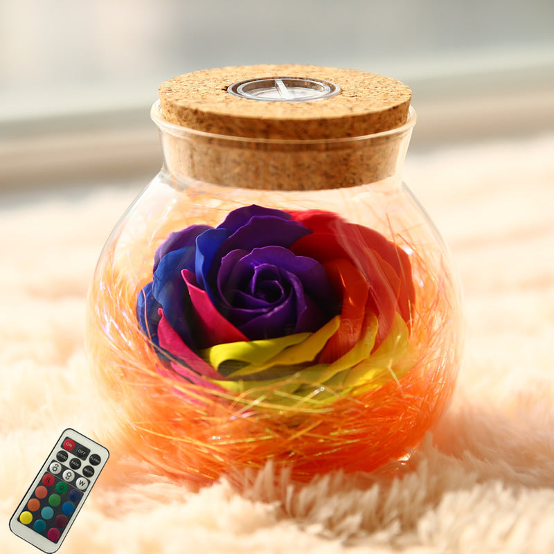 Glass jar with cork lid containing a rainbow-colored rose, placed on a soft surface with a blurred background.