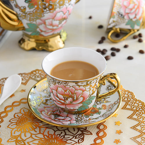 Decorative teacup with floral design on a saucer, filled with tea, on a patterned tablecloth.