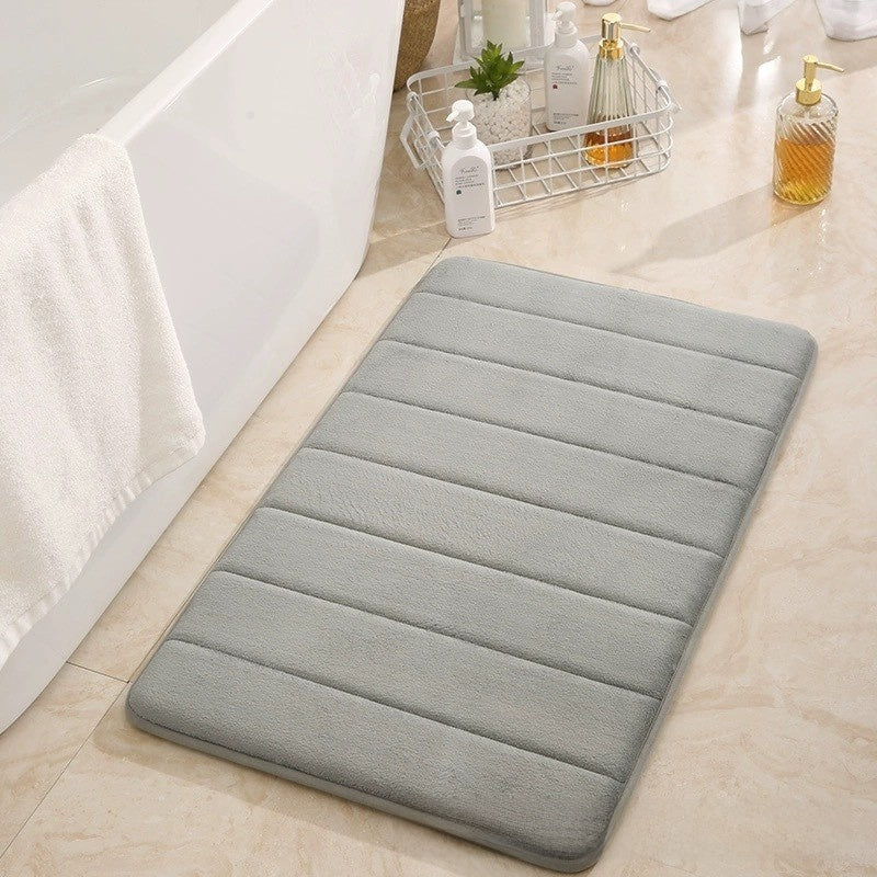 Gray bath mat on a bathroom floor with toiletries in the background