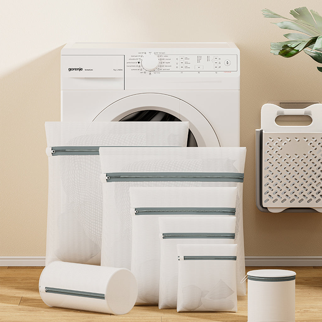 Laundry bags and a cylindrical container in front of a white dryer on a wooden floor.