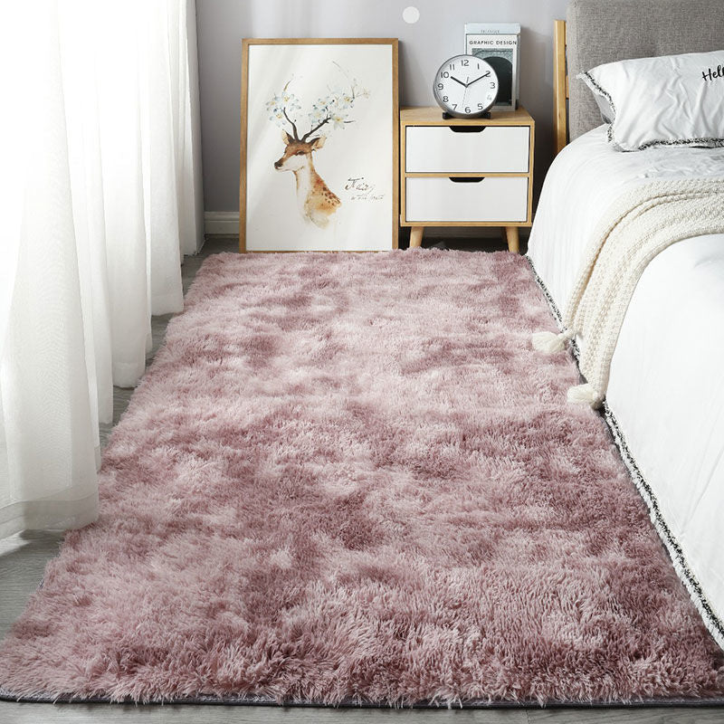 Pink shaggy rug in a bedroom setting with a bed, nightstand, and wall art.