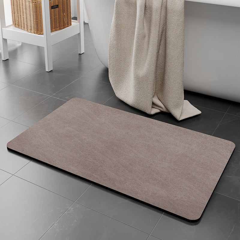 Brown bath mat on a gray tiled bathroom floor with a towel draped over a bathtub.