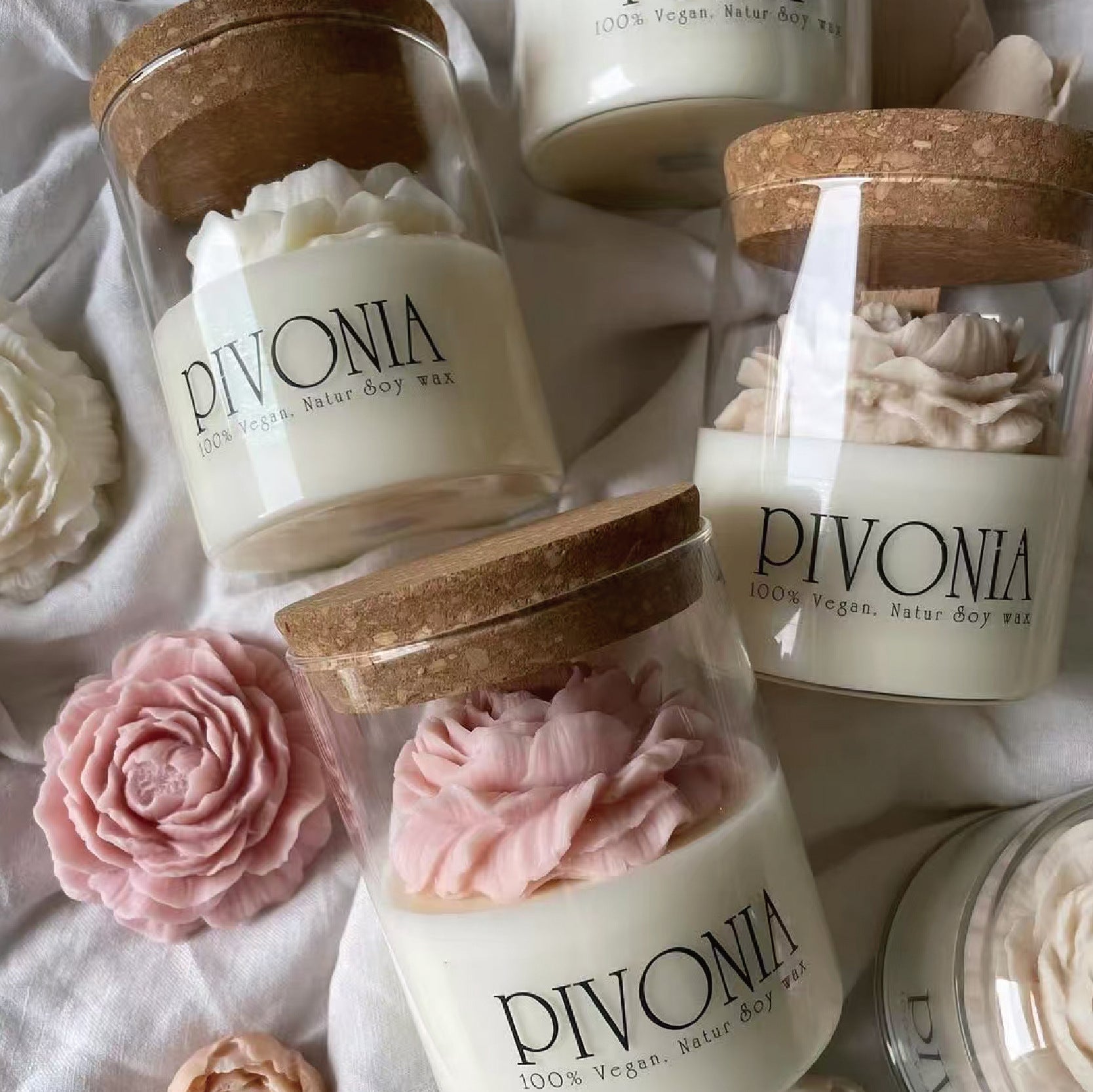 Pivonia candles with wooden lids and floral designs on a soft fabric background