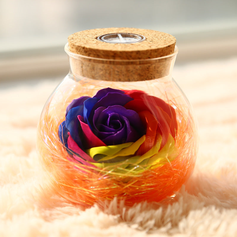 Glass jar with cork lid containing a colorful rose and twine on a soft surface.