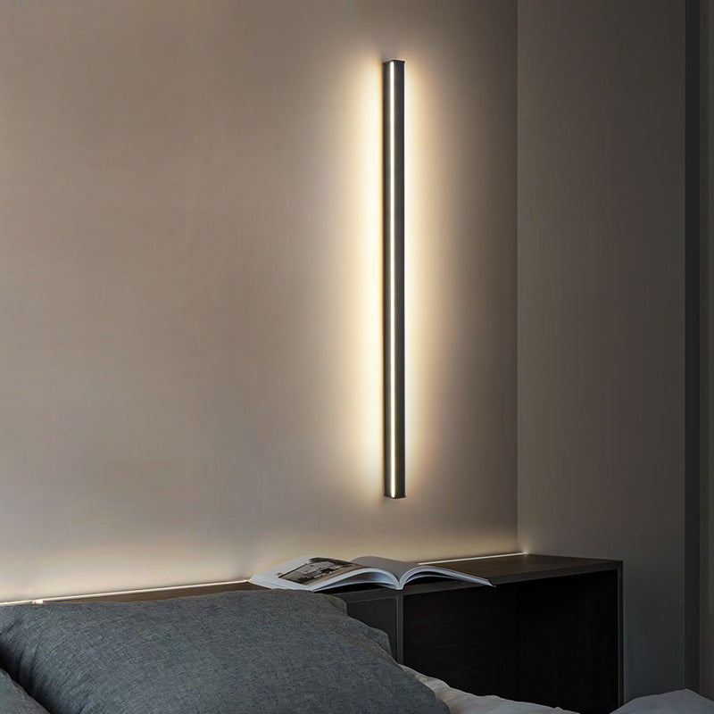 Modern wall-mounted light fixture on a neutral wall above a bed.