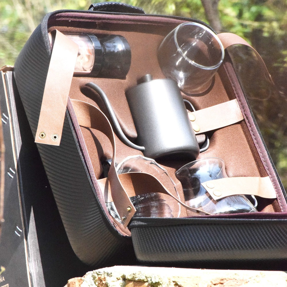 Open suitcase with a wine set including glasses and a flask, outdoors.