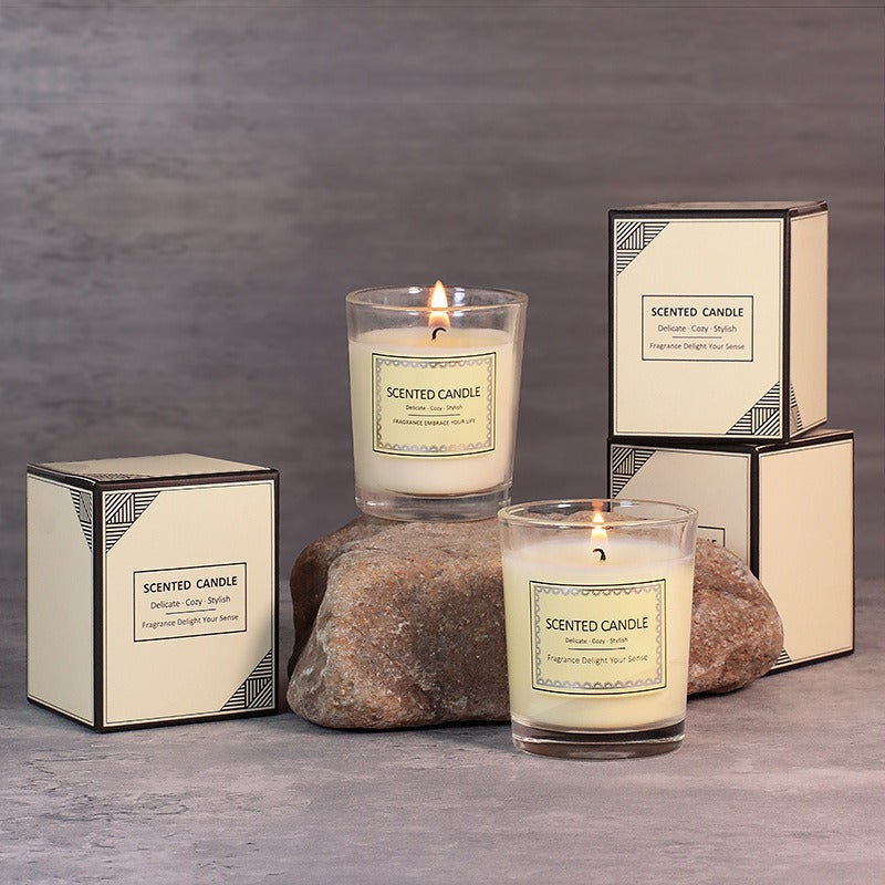 Two lit scented candles with their packaging on a gray surface and background.