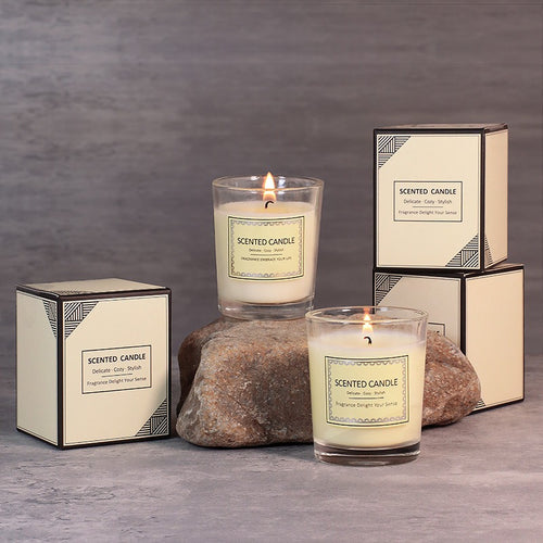 Two lit scented candles with their packaging on a gray surface and background.
