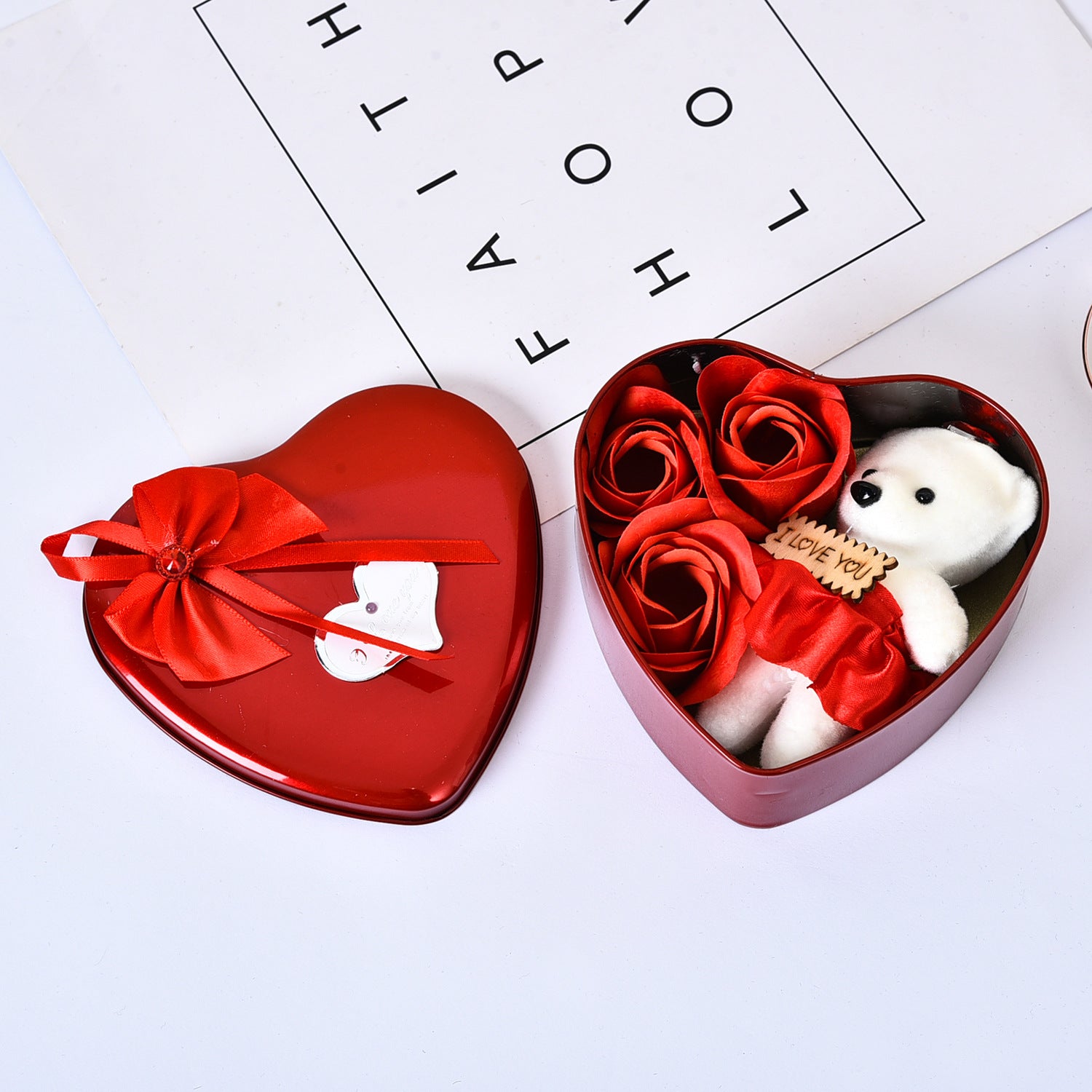 Heart-shaped gift box with red roses and a white bear toy on a white background.