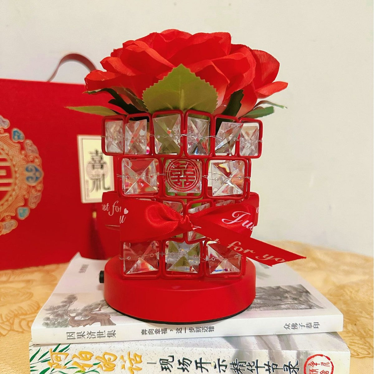 Decorative red vase with flowers on a stack of books, with a red box in the background.