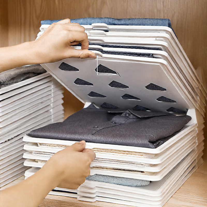 Person using a folding board to stack folded clothes neatly on a wooden surface