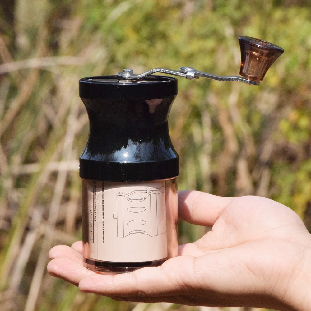 Hand holding a black manual coffee grinder with a blurred natural background