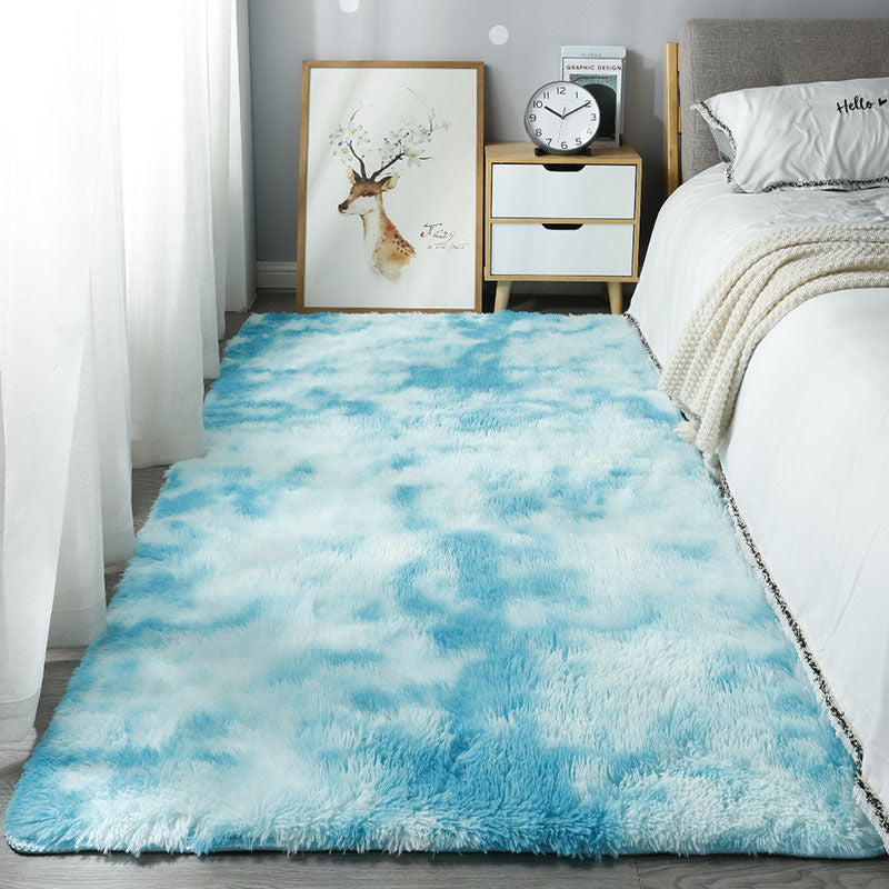 Blue and white cloud-patterned rug in a bedroom setting with a bed and nightstand.