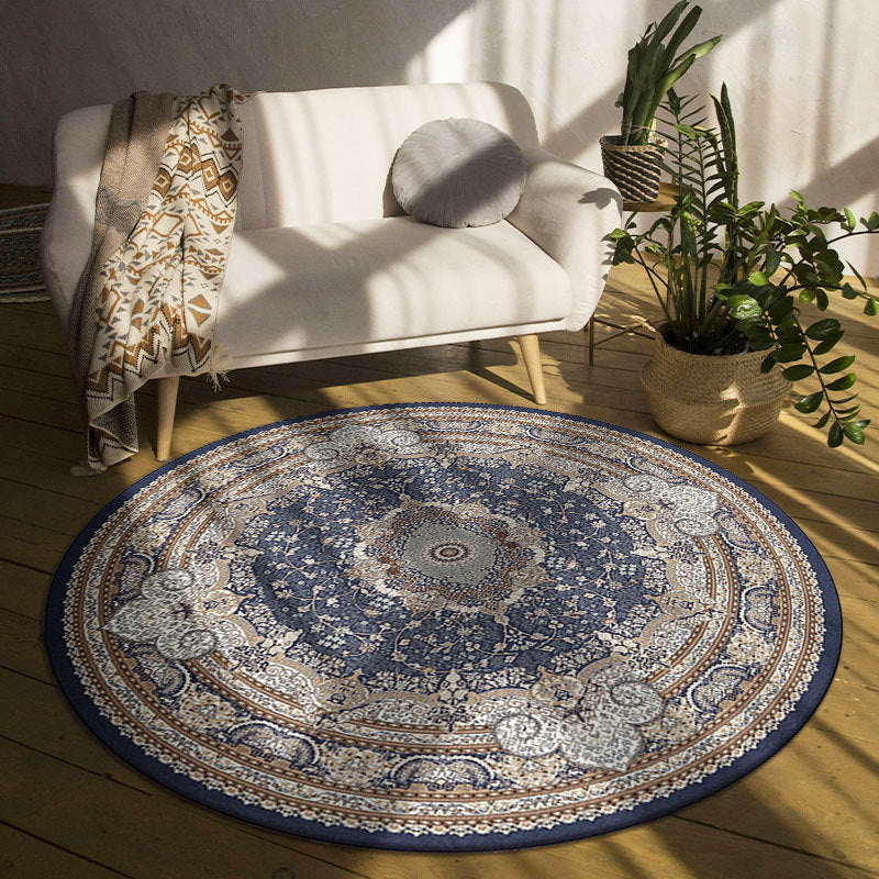 Round blue patterned rug in a room with a white chair, plants, and a wooden floor.