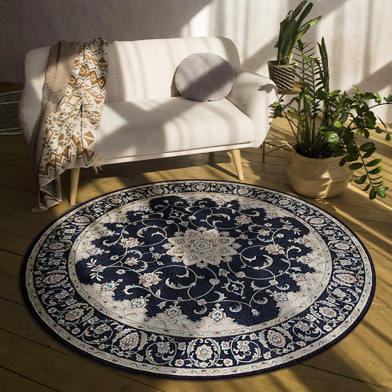 Round decorative rug with intricate patterns on a wooden floor in a room with a white sofa and plants.
