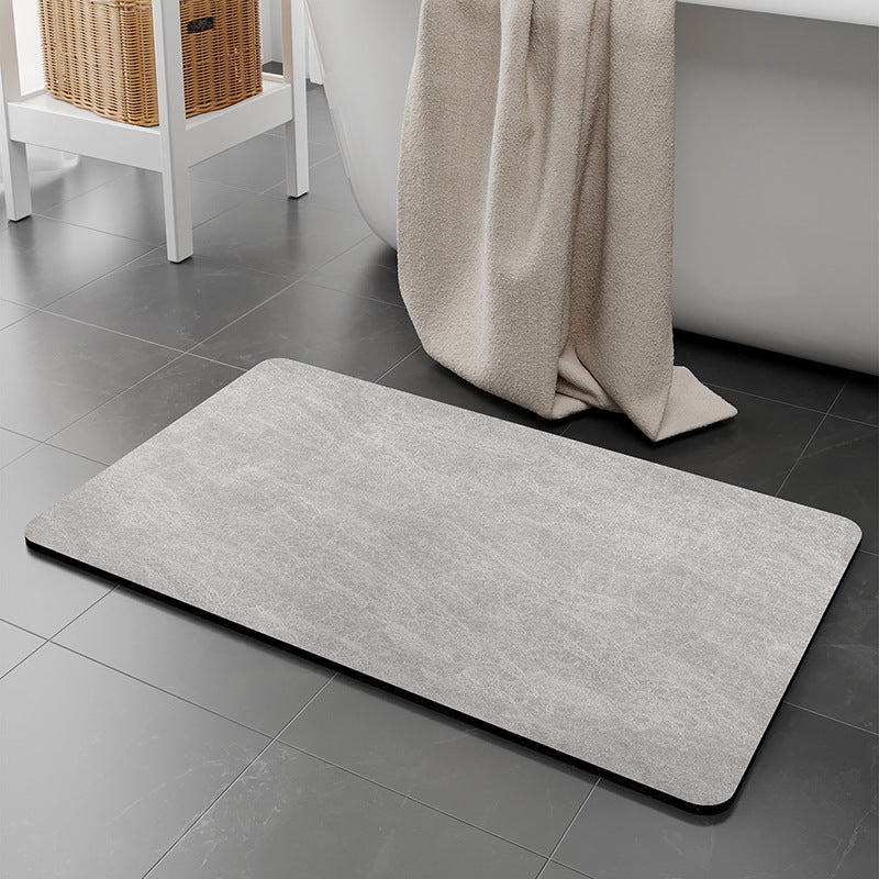 Gray bath mat on a tiled bathroom floor with a towel draped over a bathtub.