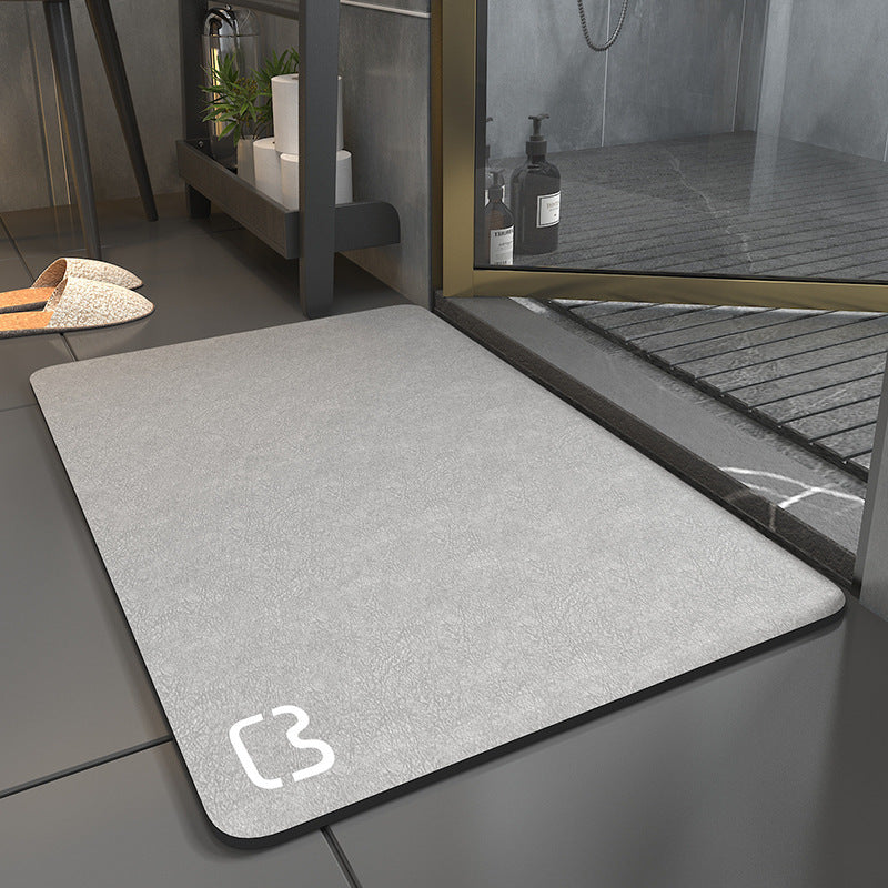Gray doormat with a brand logo on a tiled floor next to a glass door.