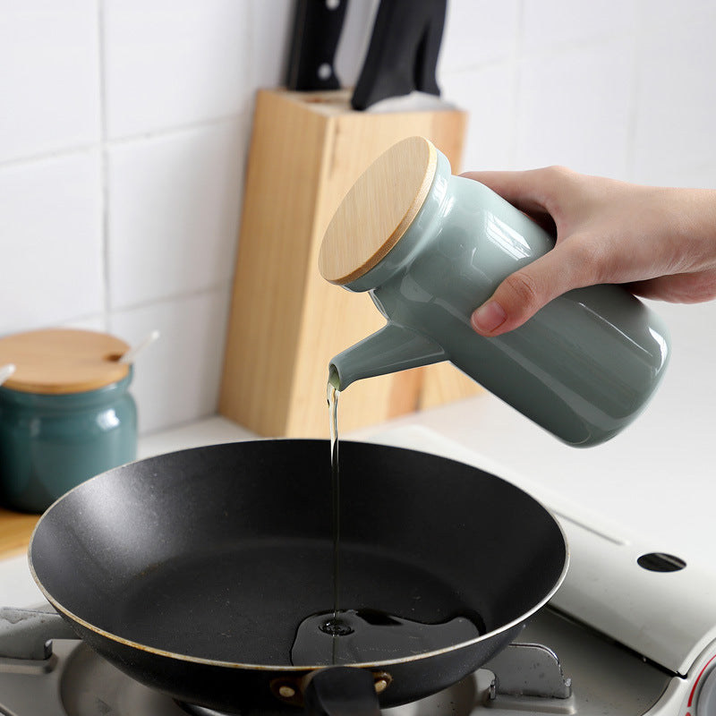 Person pouring oil from a green ceramic bottle into a black frying pan on a stove.