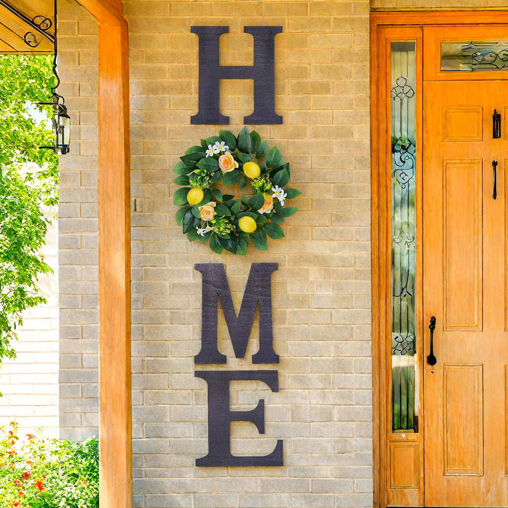Decorative wreath with flowers and greenery on a brick wall with 'HOME' letters.
