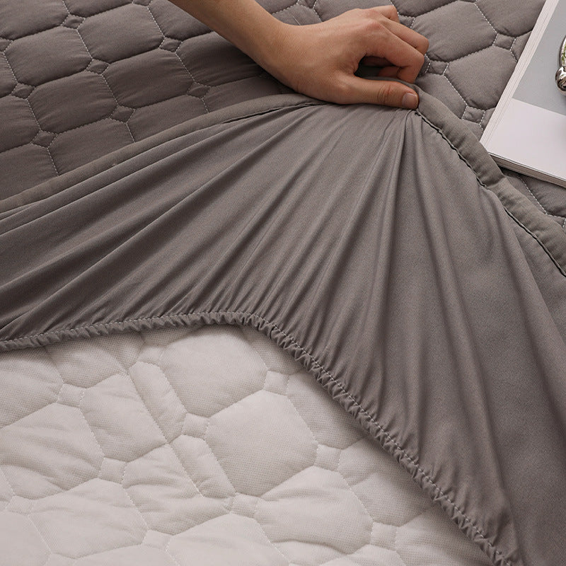 Gray quilted mattress cover with a hand adjusting it on a bed.