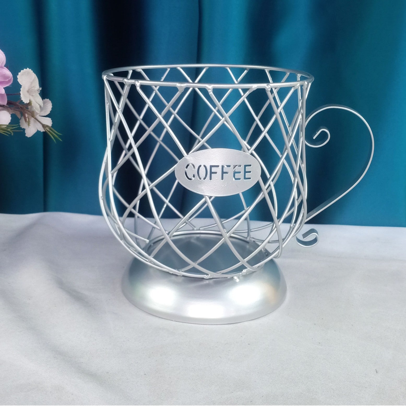 Metallic wire  coffee capsules holder with 'COFFEE' label on a white surface and blue background