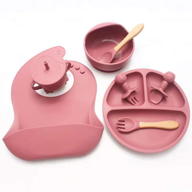 Pink silicone dining set with plate, bowl, and utensils on a white background