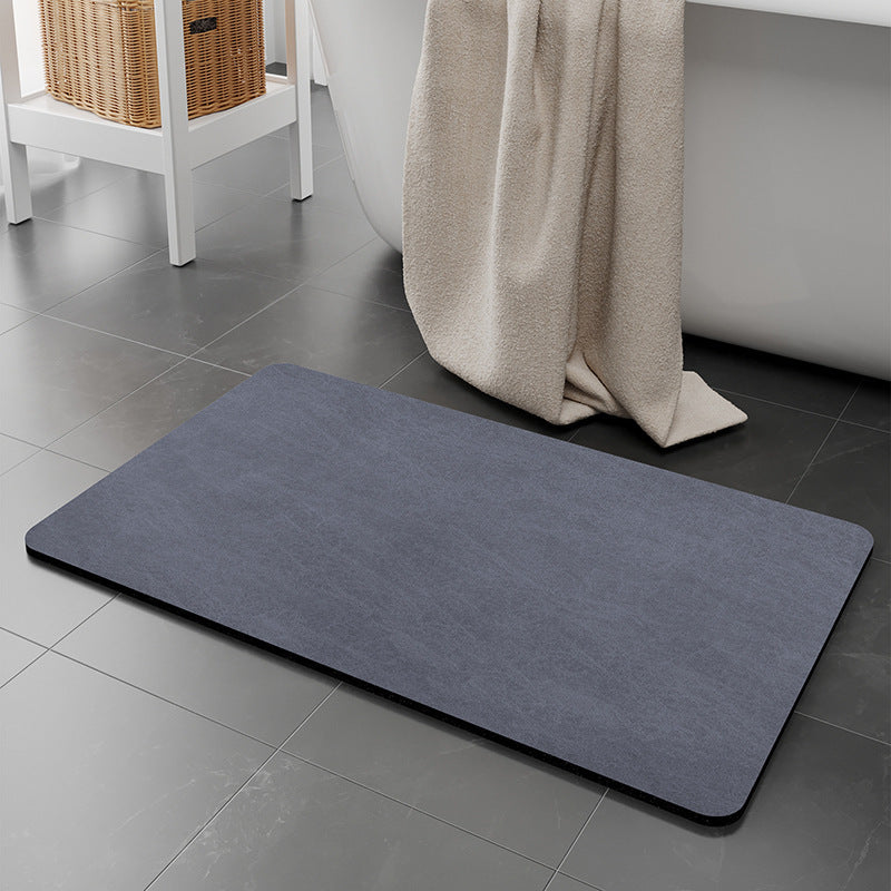 Gray bath mat on a tiled bathroom floor with a towel draped over a bathtub.