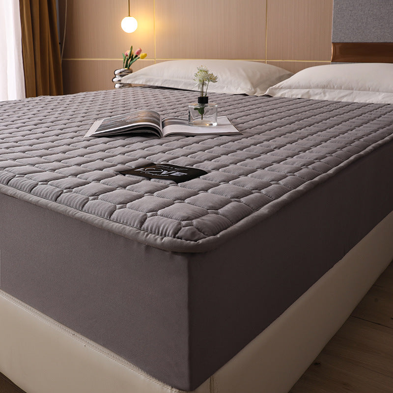 Gray quilted mattress topper on a bed with a book and remote control.