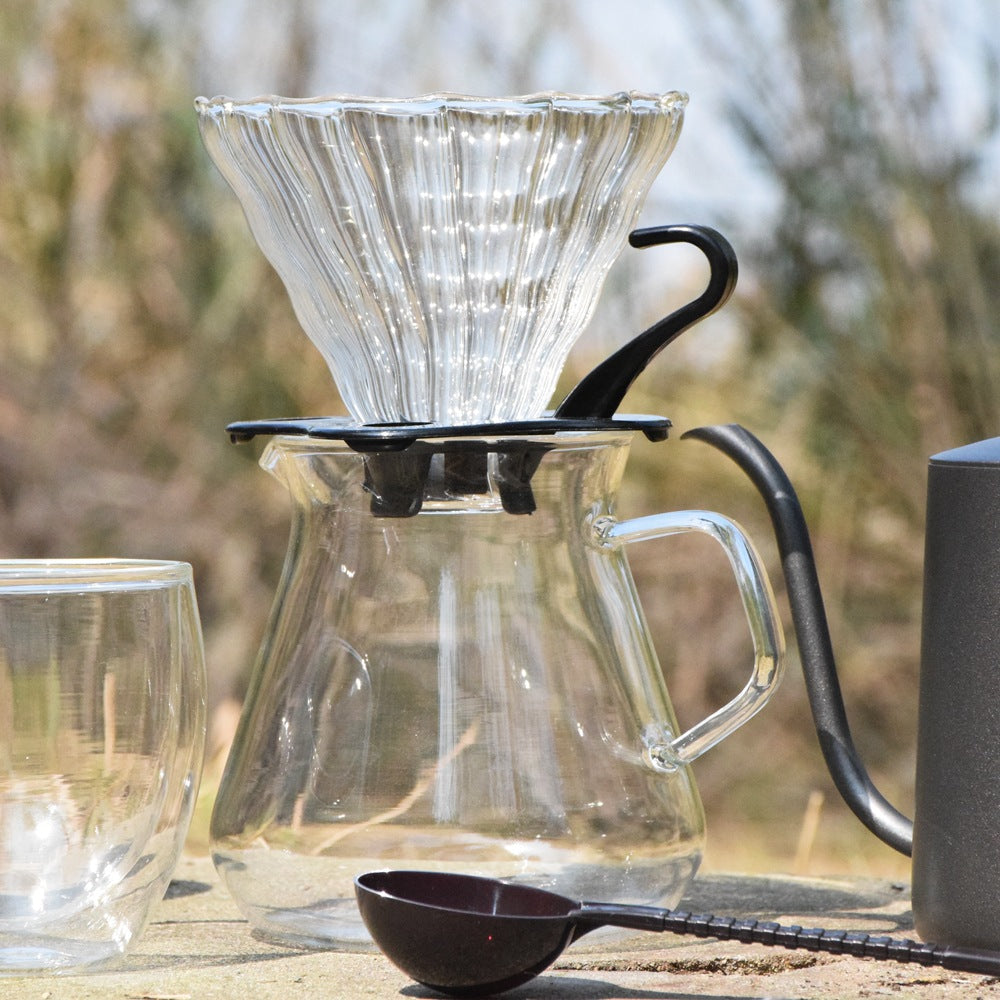 Clear glass coffee maker with black handle on a wooden surface outdoors