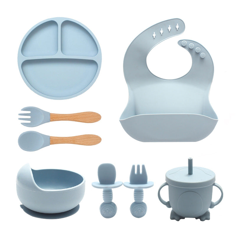 Collection of baby feeding utensils including a plate, bib, spoons, and cups on a white background.