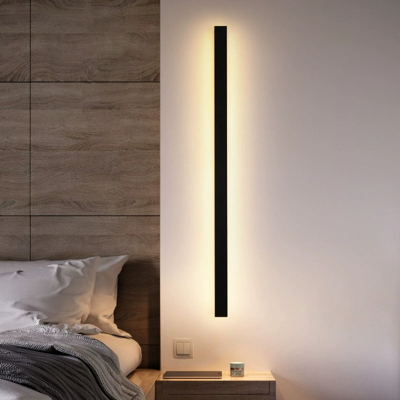 Modern wall-mounted light fixture in a bedroom setting with wooden headboard and nightstand.