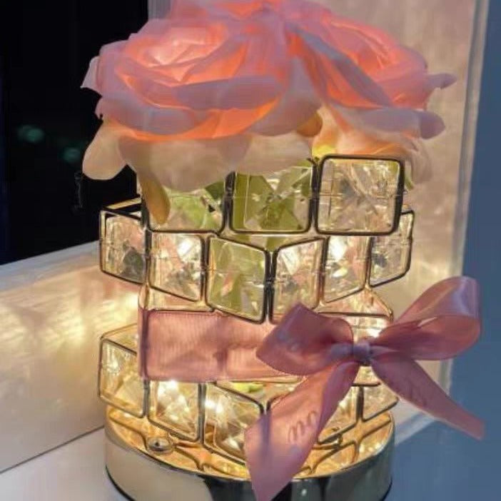 Decorative lamp with floral design and pink ribbon on a reflective surface.