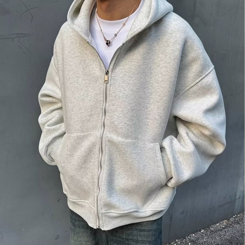 Person wearing a light gray hoodie against a dark gray wall