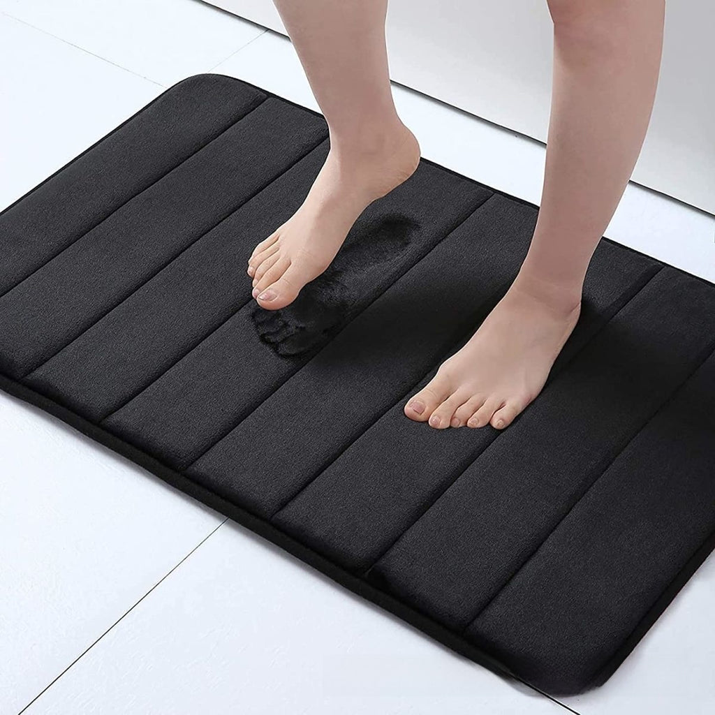 Black cushioned mat with feet stepping onto it on a light-colored floor.