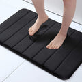 Black cushioned mat with feet stepping onto it on a light-colored floor.
